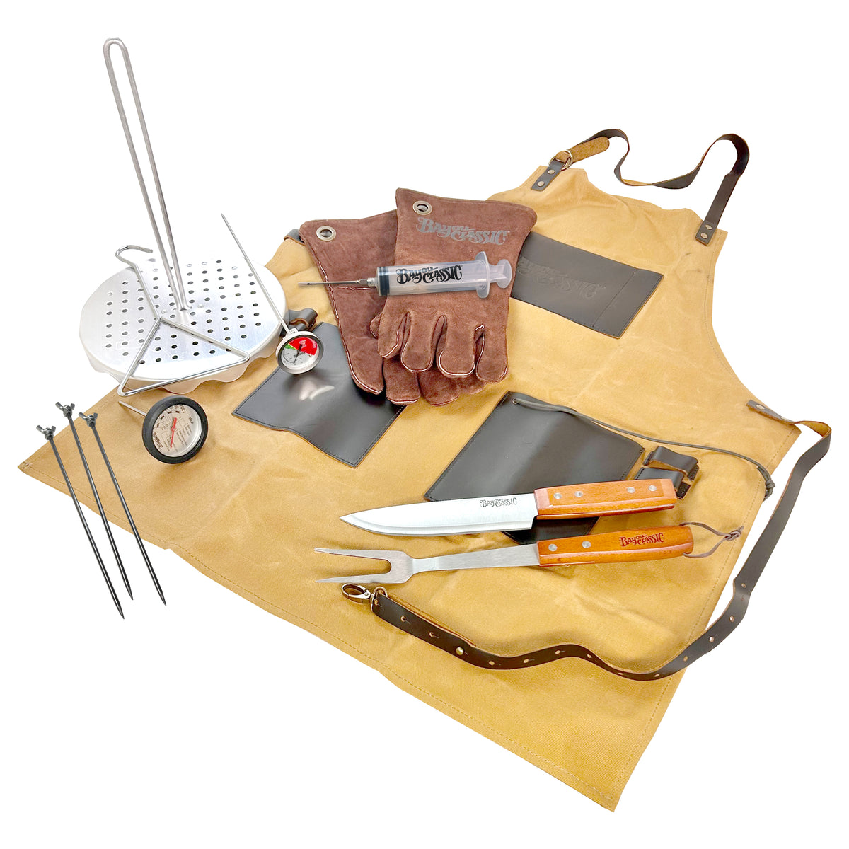 A set of poultry cooking tools including a perforated poultry rack, lift hook, leather gloves, seasoning injector, thermometers, chef's knife, fork, and an apron laid out on a white background.