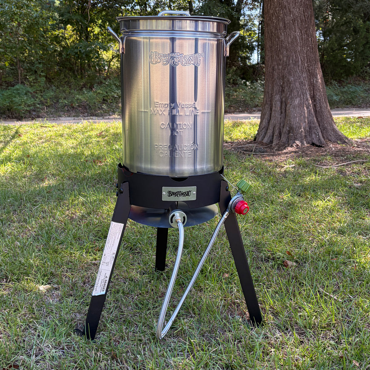 A stainless steel turkey fryer pot on a steel  cooker in an outdoor setting.