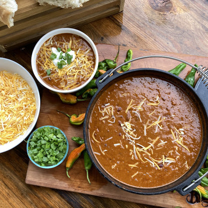 Chili with cheese and green onions in a Cast Iron Dutch Oven on a wooden table