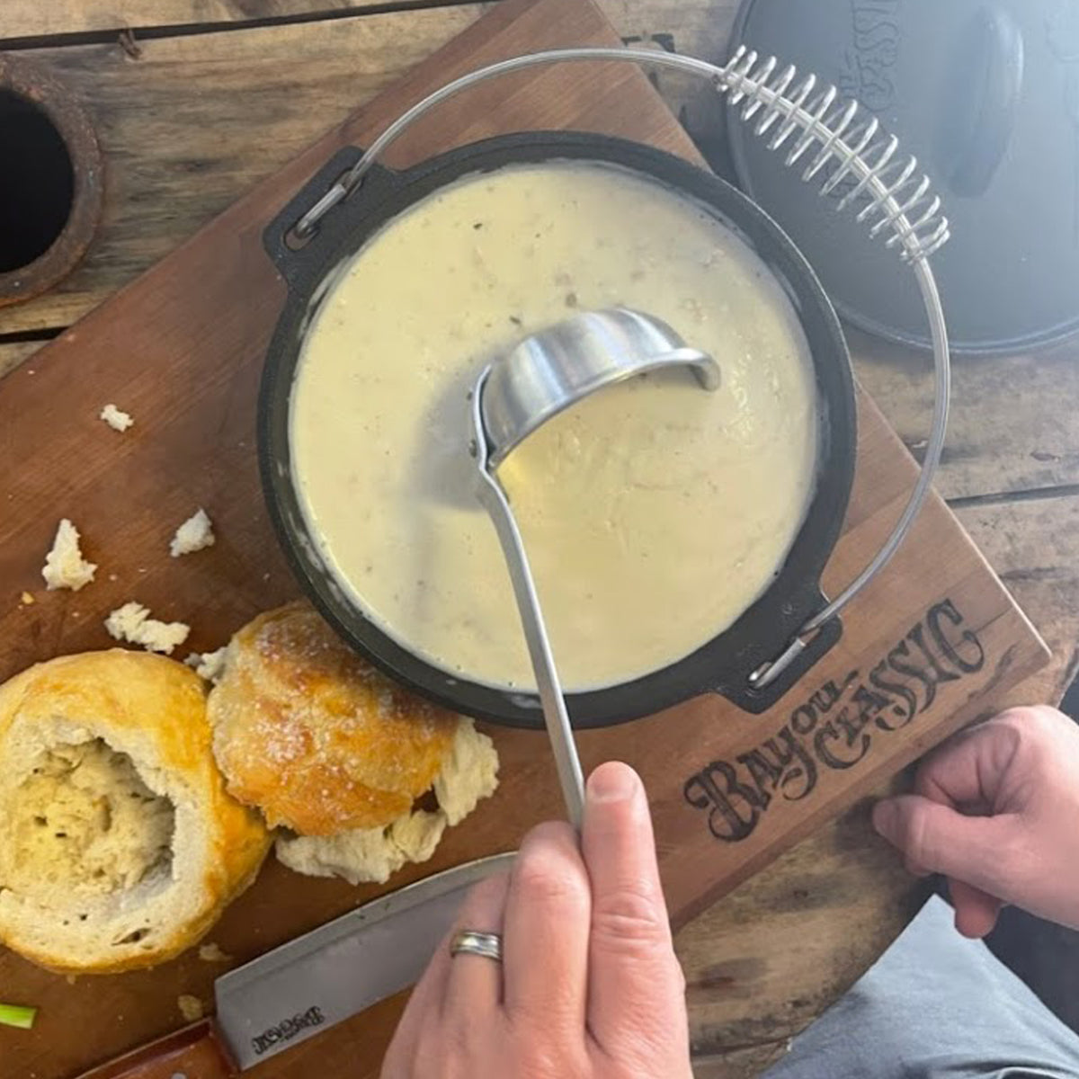 Cast Iron Soup Pot with chowder being served with bread on a wooden board.