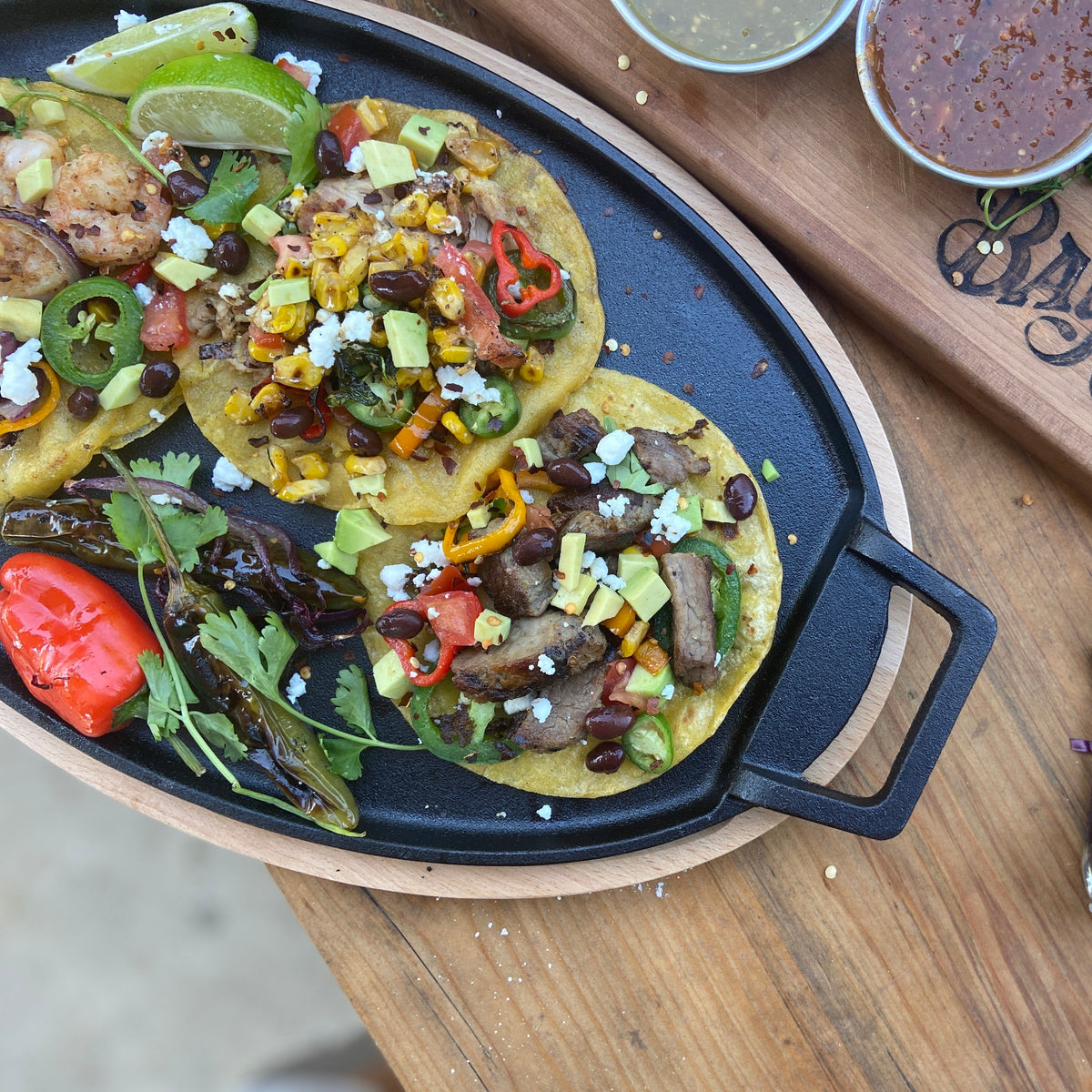 Cast iron fajita pan on a wooden trivet with corn street tacos with colorful ingredients.