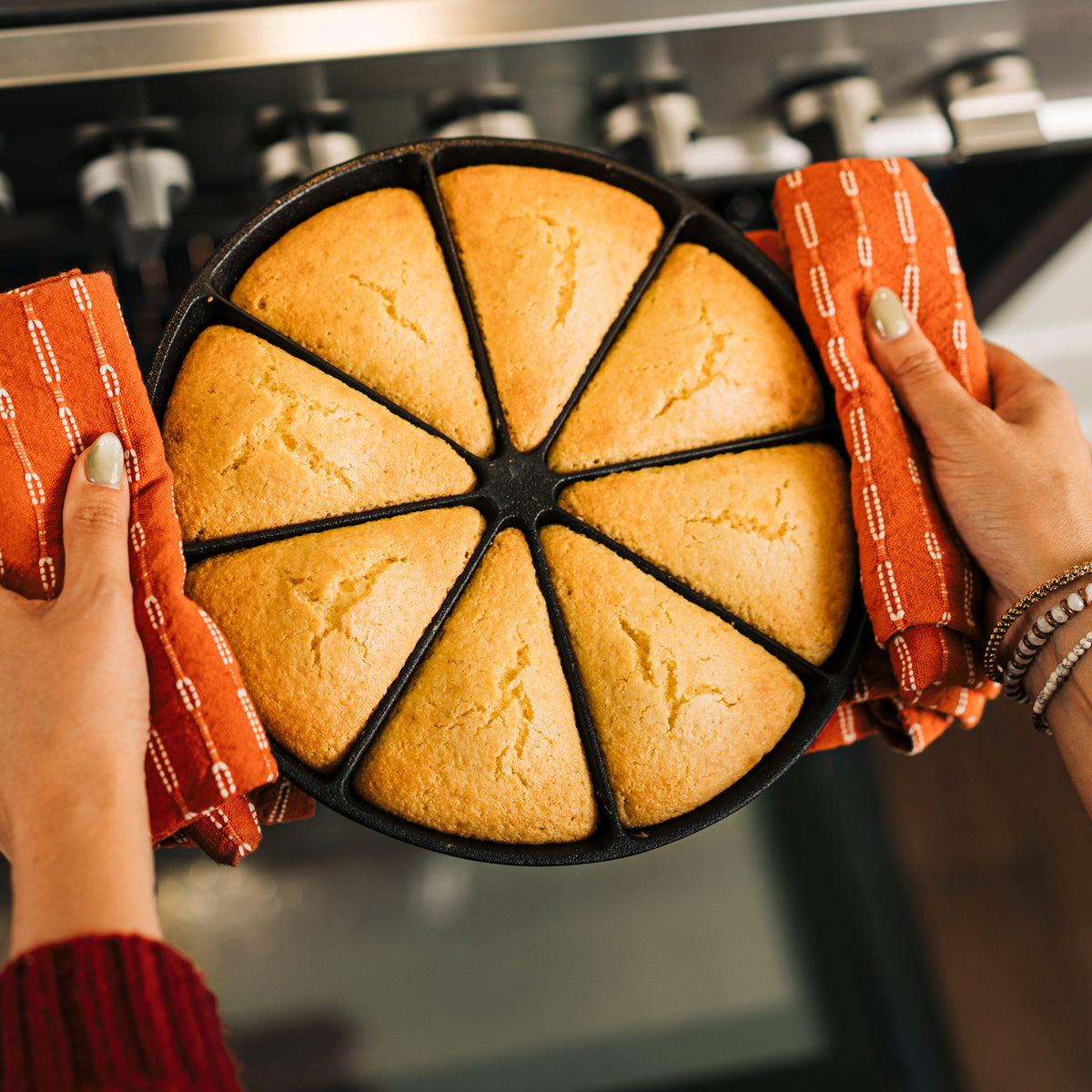 Person holding a cast iron pan with baked cornbread wedges in front of an oven.