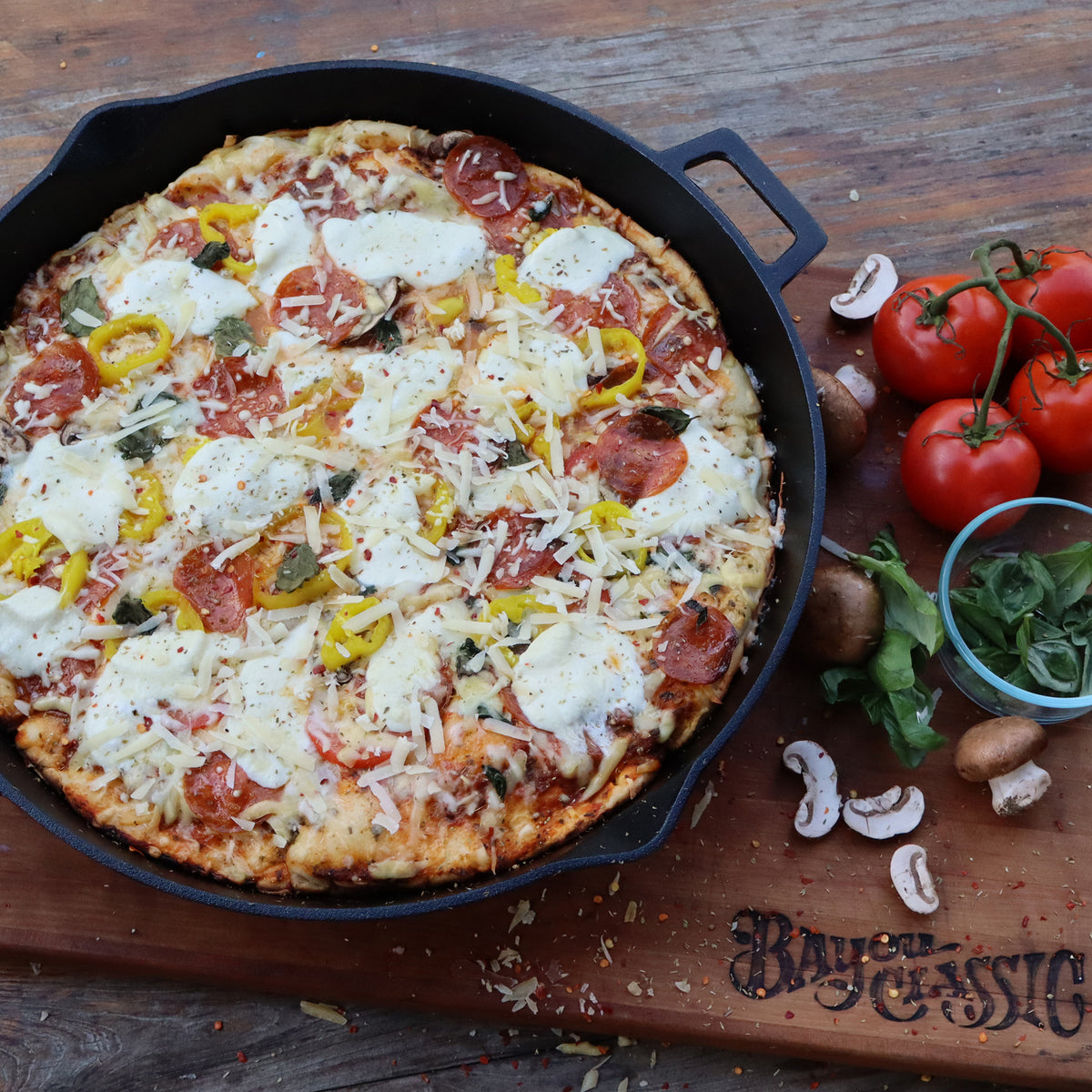 Personal pizza with various toppings in a cast iron skillet on a wooden board with fresh ingredients.